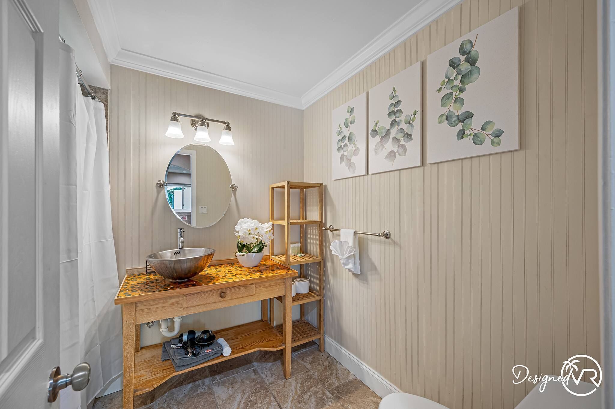 A bathroom with a wooden vanity, a round mirror, and a sink. There are three wall-mounted shelves and a towel rack.