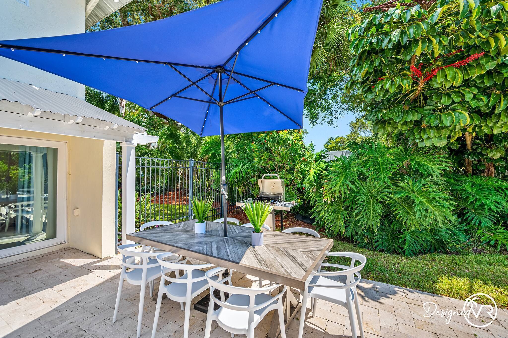 An outdoor patio with a table and chairs, a blue umbrella, and a grill.