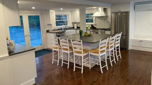 Una cocina moderna con una isla central, armarios blancos y un ventanal con vistas al exterior.