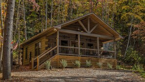 A wooden cabin with a porch and a staircase, surrounded by trees with autumn foliage. - Relaxing Getaway! Cozy Log Cabin, Hot Tub + Firepit (Cherry Log)