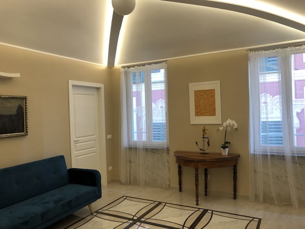 Relax in this serene living room with a sofa, table, and artwork, surrounded by sheer curtains and a minimalist design.