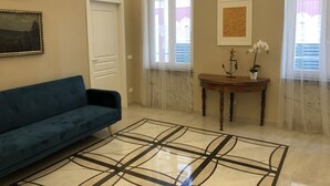 A living room with a blue sofa, a marble-patterned rug, a wooden table with a vase of flowers, and a framed artwork on the wall. - Camogli Eden Luxury - spacious and cozy apartment by the sea (Camogli)