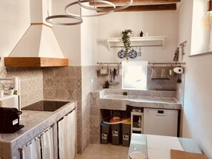 Ett kompakt kök med en inbyggd spis, en hängande lampa och ett fönster ovanför diskbänken.