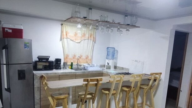 A modern kitchen with a central island, wooden bar stools, a refrigerator, a coffee maker, and a water dispenser. - San San Andrés Magic House 0 by BBBSAI (San Andrés)