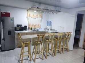 A modern kitchen with a central island, wooden bar stools, a refrigerator, a coffee maker, and a water dispenser. - San San Andrés Magic House 0 by BBBSAI (San Andrés)