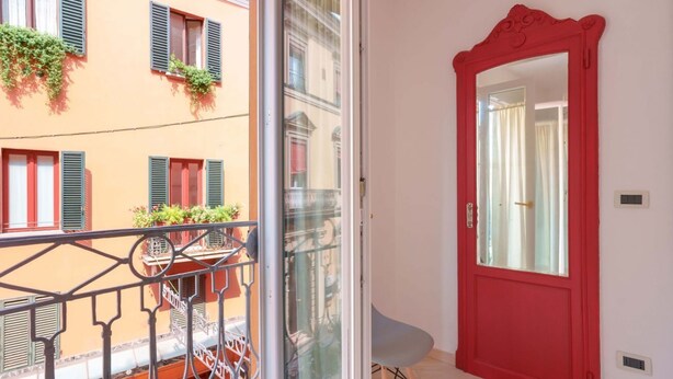 Un balcon avec une balustrade en métal, une porte rouge et une petite chaise.