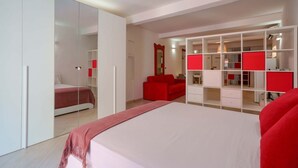 Une chambre moderne avec un grand lit, un canapé rouge et une armoire blanche aux portes miroir.