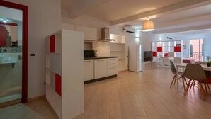 Une cuisine moderne avec des meubles blancs et des touches de rouge, un coin repas avec une table et des chaises, et une grande fenêtre qui laisse entrer la lumière naturelle.
