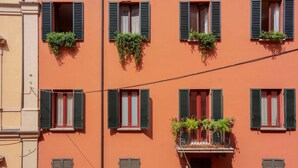 Un immeuble doté de nombreuses fenêtres, dont certaines sont équipées de volets, et de balcons ornés de plantes.