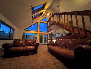 A spacious living room with a high ceiling, large windows, a wooden staircase, and leather sofas. - Window of the Rockies! (Bailey)