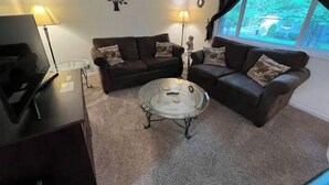 A living room with two sofas, a glass coffee table, and a TV on a stand. - Cozy Retreat in the Woods & Gateway to Adventure (Skandia)