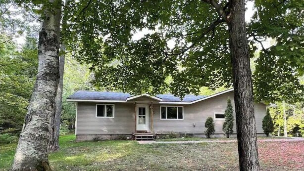 A single-story house with a front porch, surrounded by trees and a grassy yard. - Cozy Retreat in the Woods & Gateway to Adventure (Skandia)