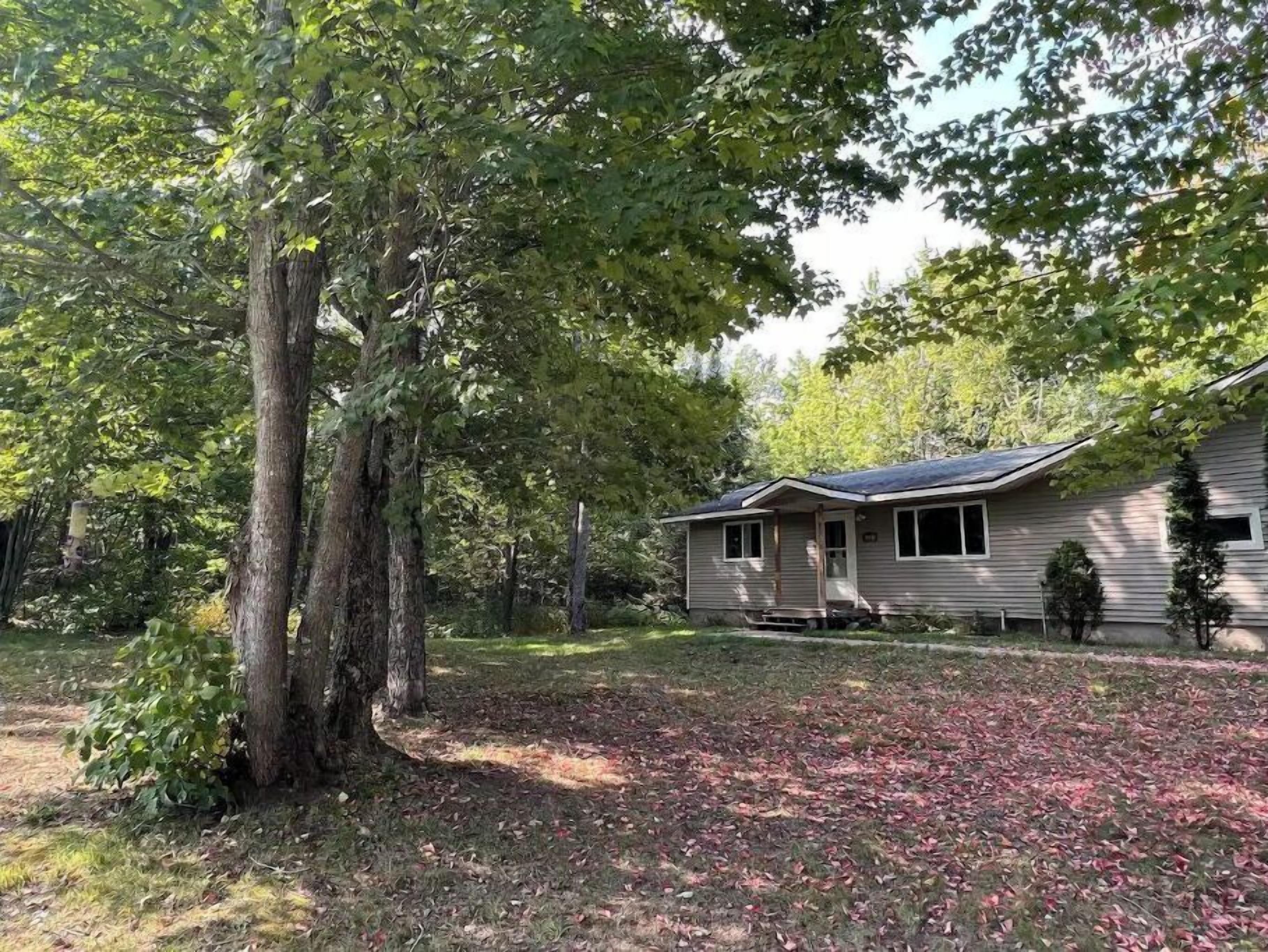 A single-story house with a sloped roof, surrounded by trees and a yard with scattered leaves.