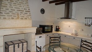 A kitchen with a stone wall, a microwave, a coffee maker, and a glass table with chairs.