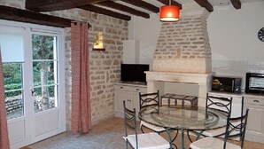 A rustic kitchen with a stone wall, a round glass table, and metal chairs.