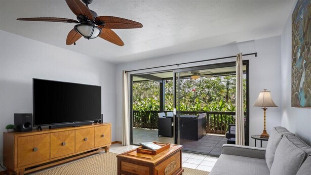 A modern living room with a flat-screen TV, wooden cabinet, sofa, and a ceiling fan. - NEW! Quiet Ocean-view 1st floor | Patio | Pool (Kailua Kona)