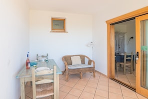 Une pièce avec une table en verre, une chaise en osier et une porte donnant sur une autre pièce.