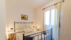 Un dormitorio con cama, mesitas de noche, un cuadro en la pared y una ventana con cortinas.