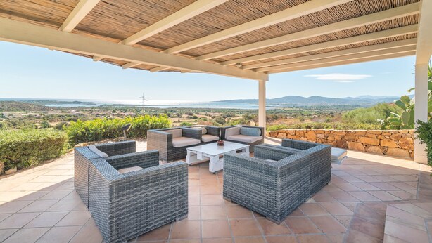 Un patio al aire libre con mobiliario de mimbre, una pared de piedra y vistas al paisaje.