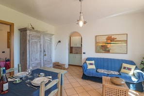 Un coin repas avec une table dressée pour deux personnes, un canapé bleu et une cuisine en arrière-plan.