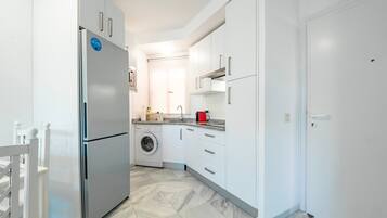 Una cocina moderna con armarios blancos, un refrigerador de acero inoxidable, una lavadora y un hervidor rojo.
