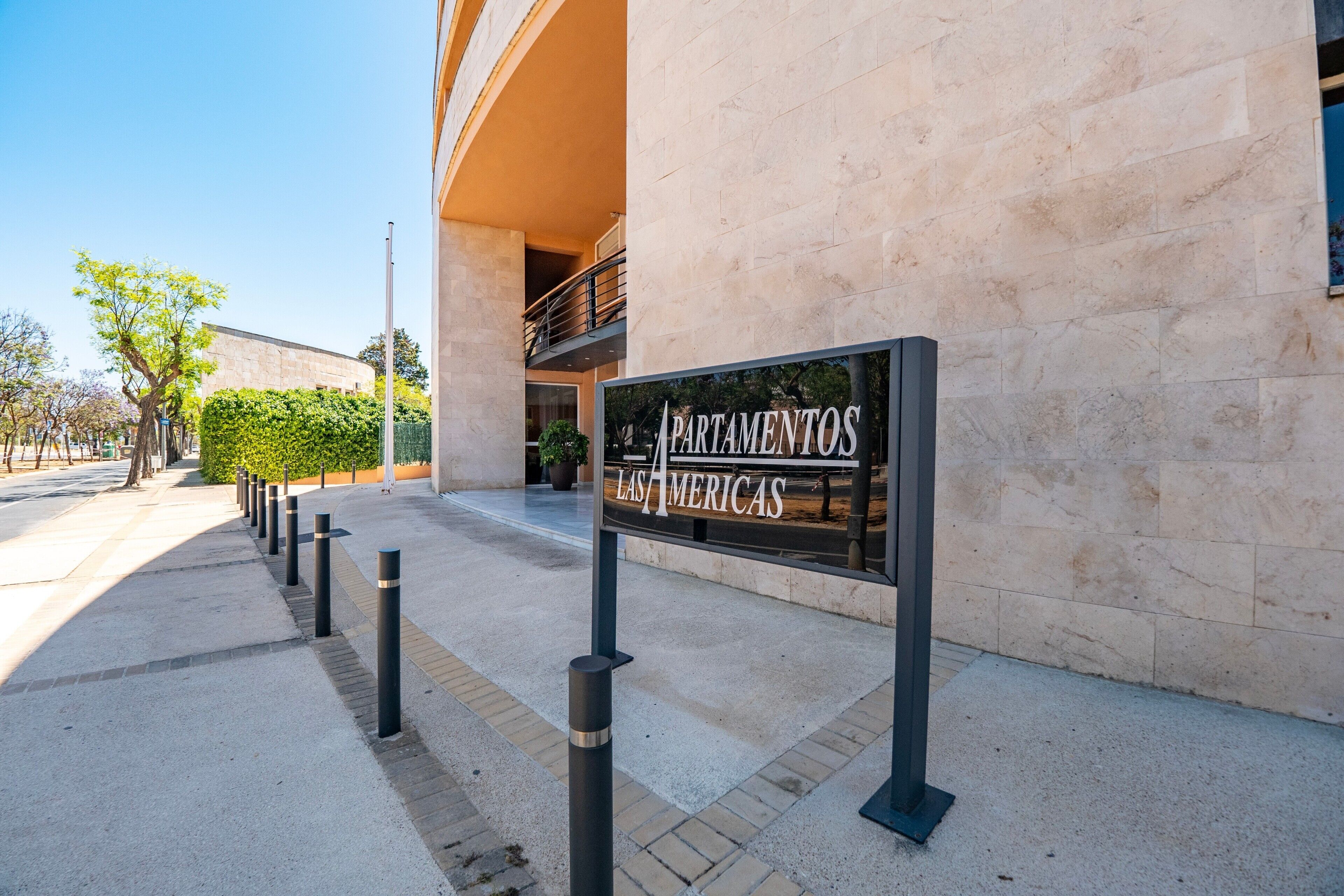 Une enseigne pour « Apartamentos Las Americas », avec la façade d’un immeuble moderne et un ciel dégagé.