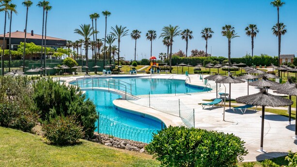 Ein Swimmingpool mit Rutsche, umgeben von Palmen und Liegestühlen.