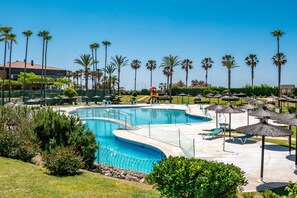 A swimming pool with a slide, surrounded by palm trees and lounge chairs. - 'Kiko Las Américas' Apartment with Sea View, Pool, and Wi-Fi (Isla Cristina)