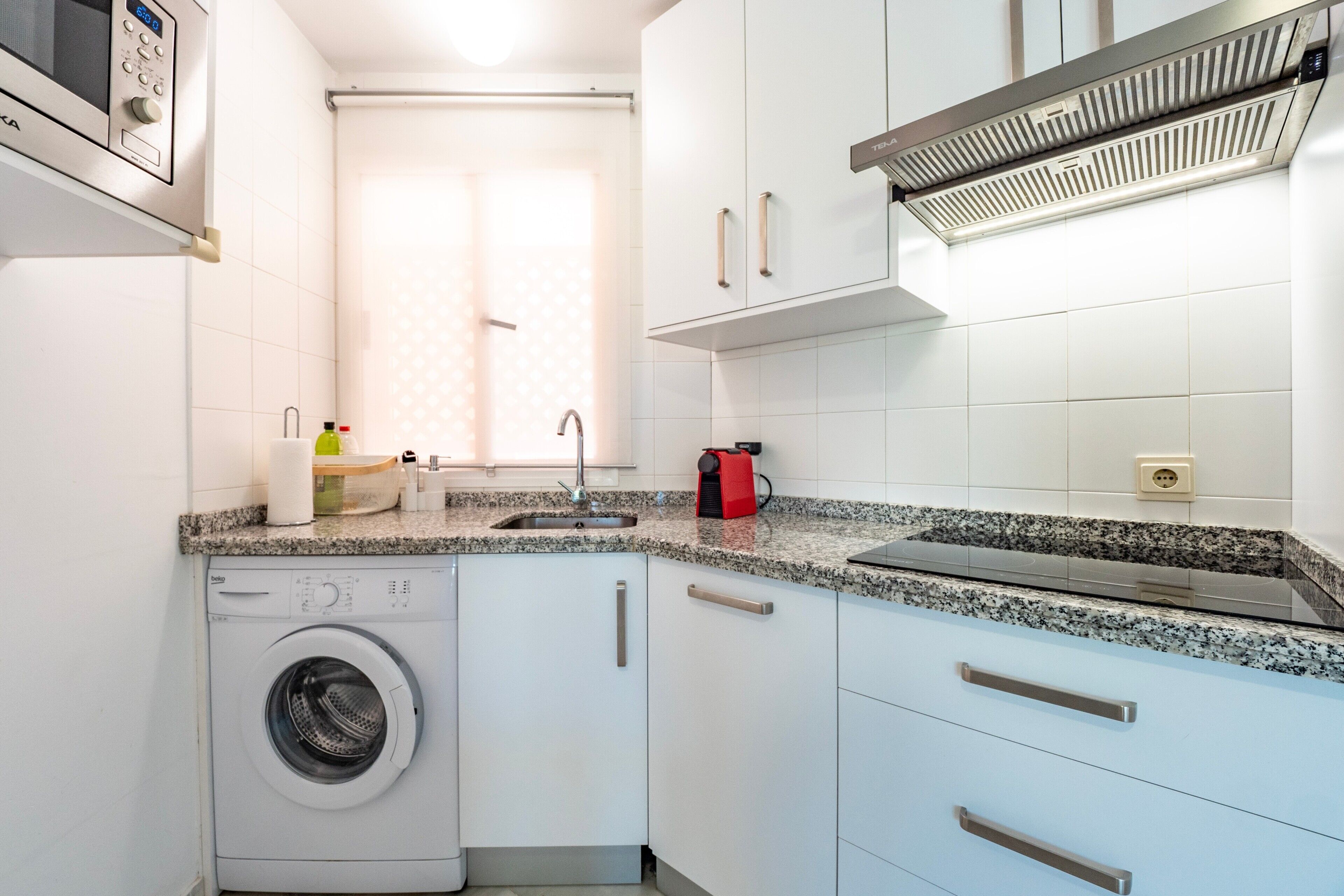 A compact kitchen with a washing machine, a sink, and a built-in microwave.