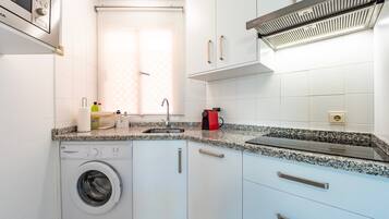 A compact kitchen with a washing machine, a sink, and a built-in microwave.