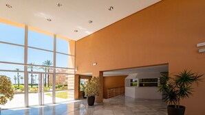 Eine geräumige Lobby mit großen Fenstern, Fliesenboden und Pflanzen in Töpfen.