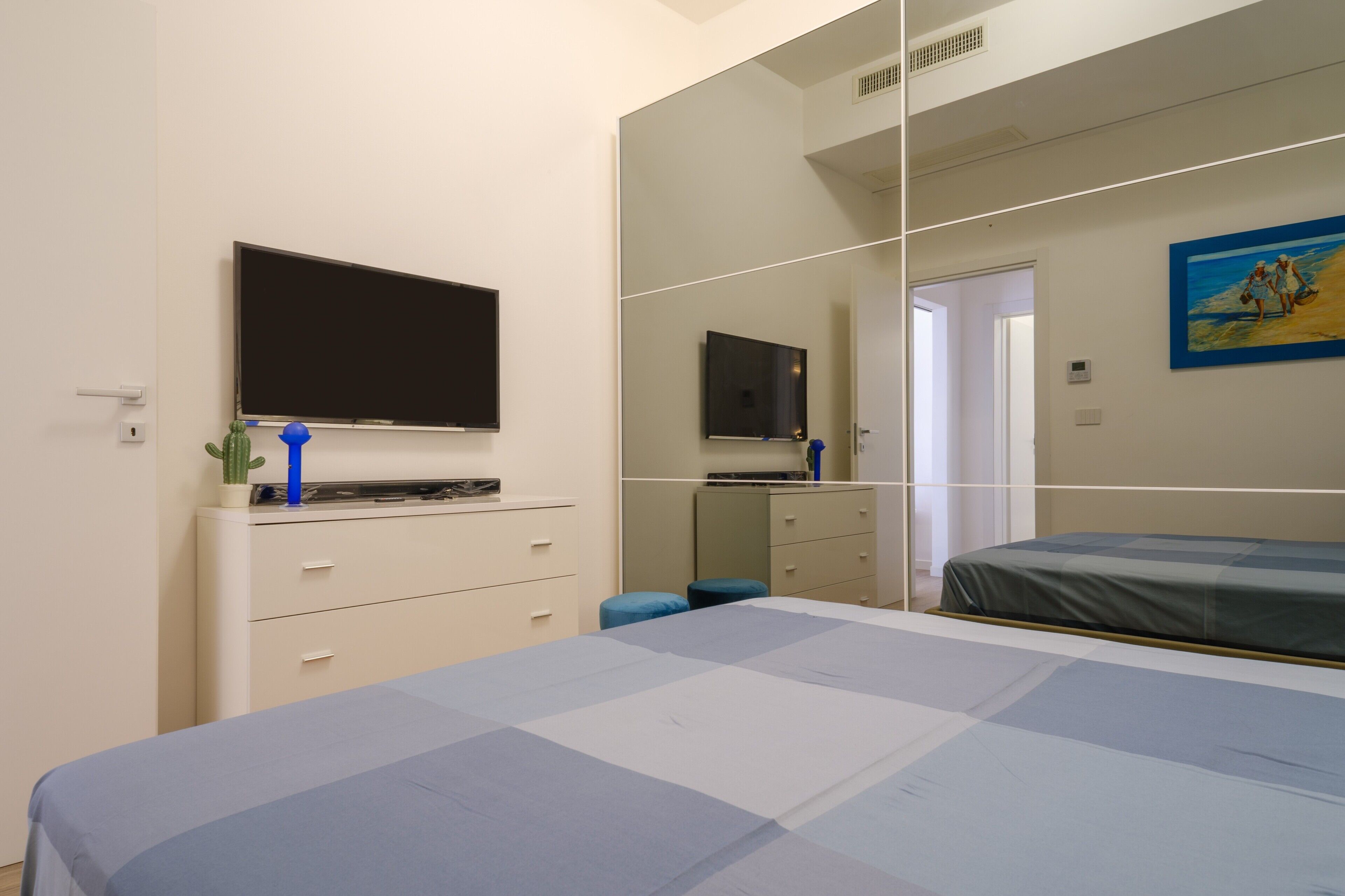 Een slaapkamer met een bed, een televisie, een spiegel en een schilderij aan de muur.