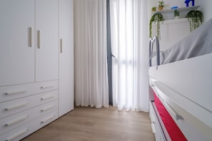 A room with a wardrobe, a bed, and a window with curtains.