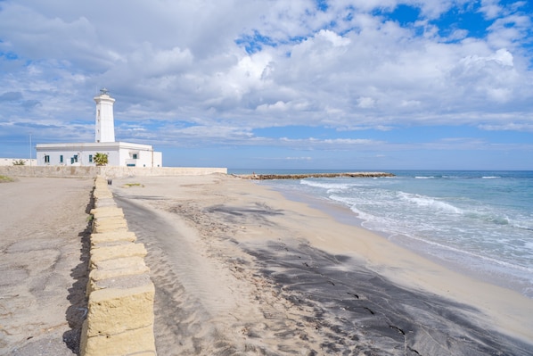 A coastal scene with a white lighthouse, sandy beach, and ocean waves.