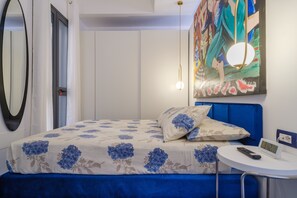 Un dormitorio con cama, mesita de noche con un reloj, un cuadro en la pared y un espejo.