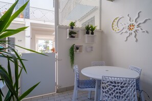 Un balcón con sillas blancas, una mesa redonda, plantas en macetas y un adorno de sol y luna.