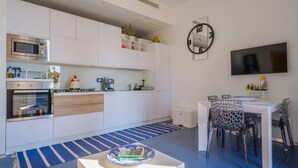 Una cocina moderna con electrodomésticos integrados, un comedor con televisor y un reloj en la pared.