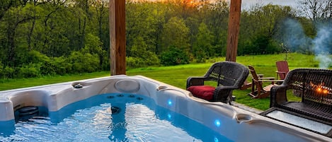 A hot tub with a view of a grassy area and trees, surrounded by wicker furniture.
