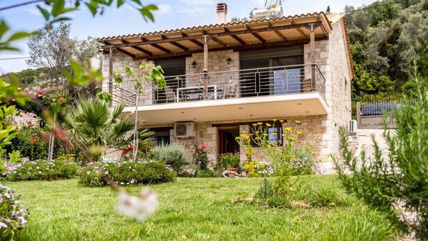 Una casa de piedra de dos pisos con un balcón, rodeada de un jardín cuidado.