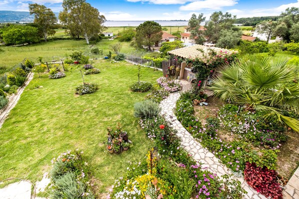 Un jardin avec un chemin en pierre, différentes plantes et un petit bâtiment doté d’un toit en tuiles.