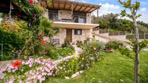 Una casa de piedra de dos pisos con un balcón, rodeada por un jardín cuidado con diversas flores y plantas.