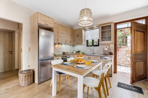 A modern kitchen with wooden cabinets, a stainless steel refrigerator, a dining table with chairs, and a wicker basket on the floor.