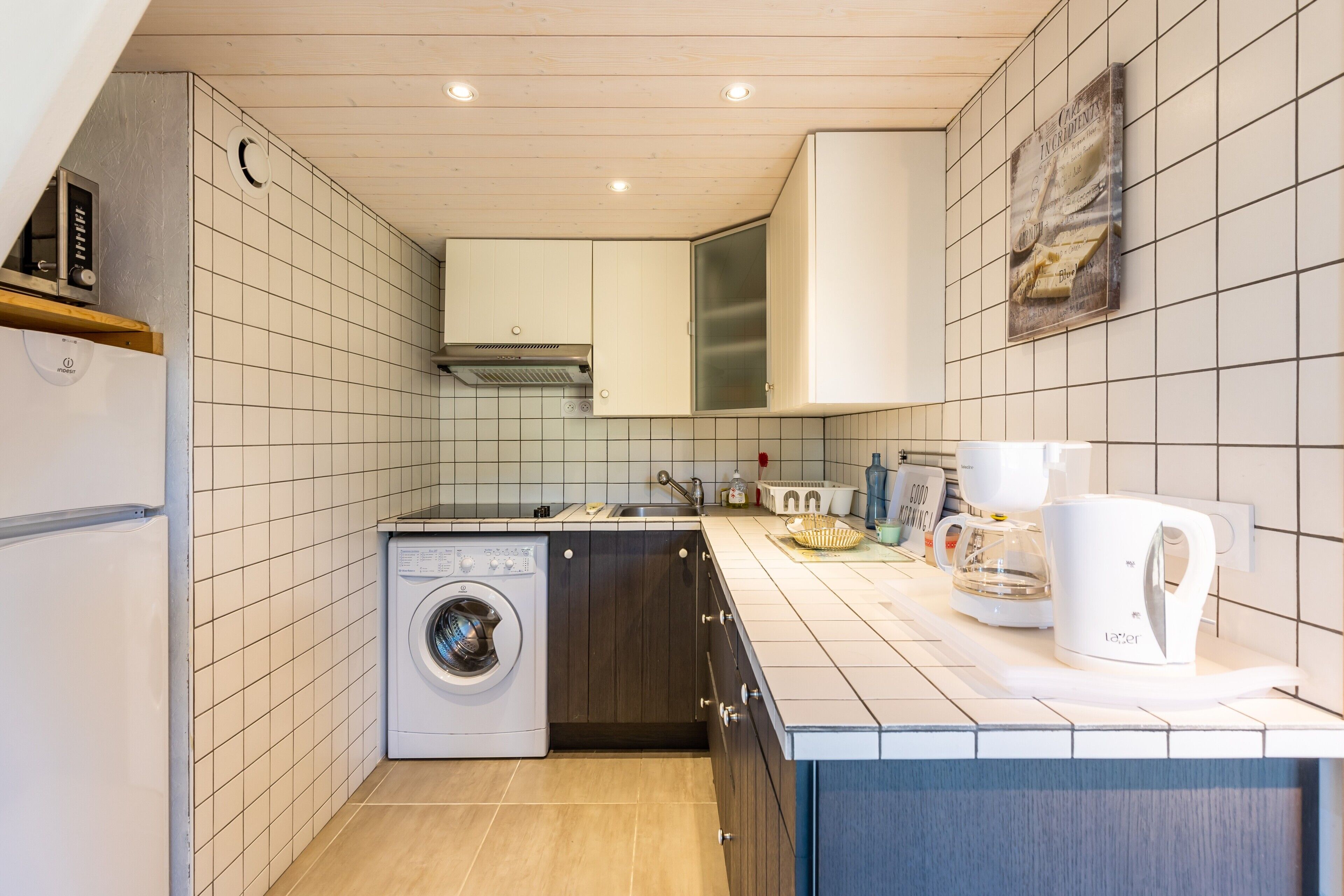 Ett kompakt kök med tvättmaskin, diskho och kaffebryggare.