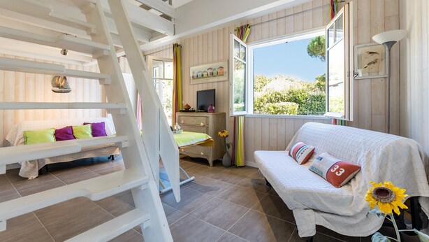 A bedroom with a bunk bed, a sofa, a TV, a window with a view, and a lamp.