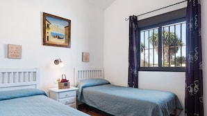 Ein Zimmer mit zwei Betten, einem Nachttisch mit Lampe, einem gerahmten Gemälde und einem Fenster mit Vorhängen.