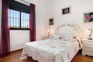 Une chambre à coucher avec un lit, des rideaux, des œuvres d’art mural et une table de chevet.