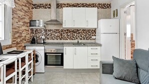 Een kleine keuken met een magnetron, fornuis, oven en witte kastjes.