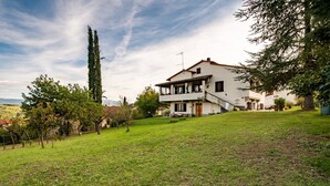 A two-story house with a balcony, surrounded by a grassy area and trees. - Holiday Home 'Tramonto sul Castello di Poppi' with View, Hot Tub, Garden & Wi-Fi (Poppi)