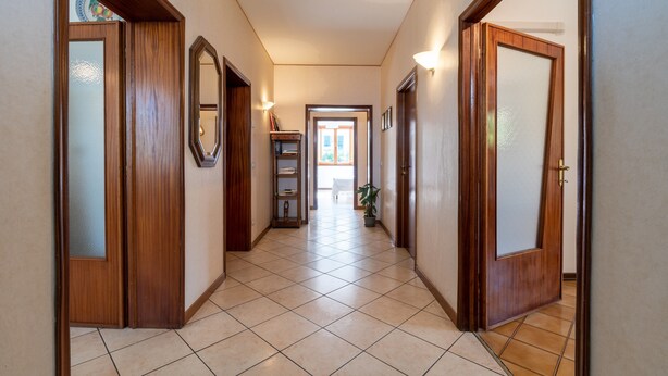 A hallway with wooden doors, a tiled floor, and a bookshelf with books and a plant. - Holiday Home 'Tramonto sul Castello di Poppi' with View, Hot Tub, Garden & Wi-Fi (Poppi)