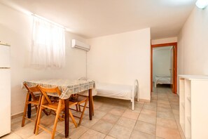 A small, single-room apartment with a dining table, chairs, a bed, and a white wardrobe.